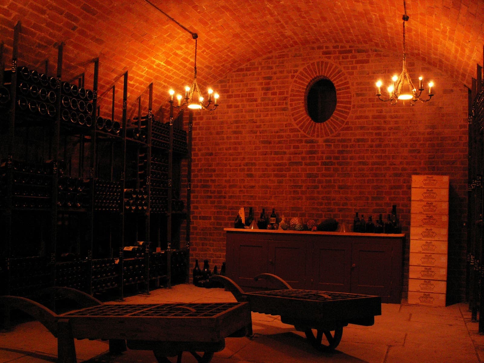 A brick-vaulted wine cellar with extensive bottle racks and warm chandelier lighting.